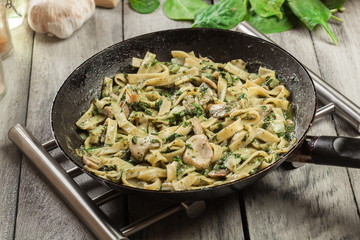 Tagliatelle pasta with spinach and mushrooms on a pan.