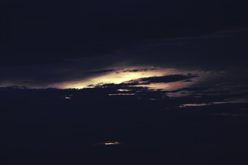 behind the clouds the dark sky the sun sets .