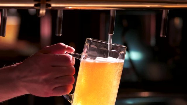 Man pours beer into a glass. Bartender's hand pouring pint of beer behind the bar. Drops of beer out of beer tap.