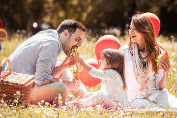 Young family with kid having picnic outdoors.