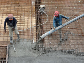 Construction workers pouring wet concrete using concrete spider hose from concrete pumping machine...