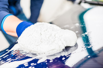 Close-up of male hand wiping the wet surface of a blue car with microfiber wash mitt for drying