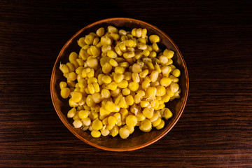 Ceramic plate with canned corn seeds on wooden table. Top view
