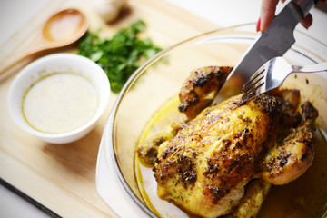 Woman hand cutting a slice from a roasted chicken on a wooden cutting board with sauce and parsley
