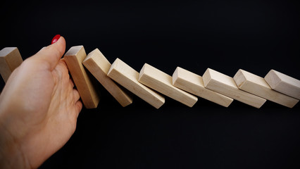 Business woman hand with red nails stopping the dominoes falling on dark background, business...