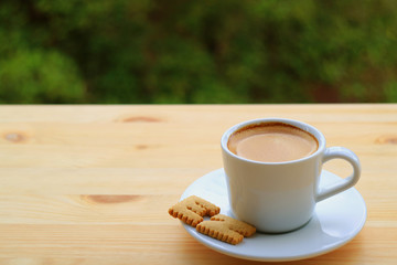 One Cup of Hot Coffee with Cookies EZ Served on Wooden Table with Blurred Green Foliage in Background 