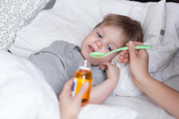 Mother giving her sick kid son cough syrup at home