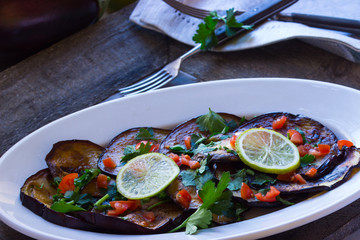 gebratene Auberginenscheiben mit Petersilie, Limonen und Tomaten als Vorspeise auf einer Platte angerichtet
