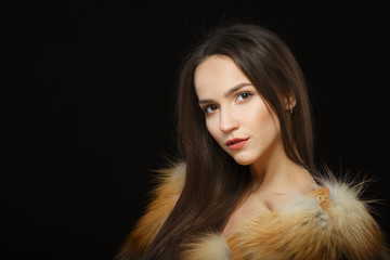 Portrait of beautiful girl with natural makeup in fluffy fur coat on black background