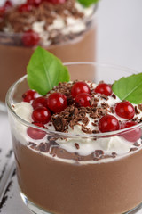Chocolate mousse with currant and mint in a glasses on a whiite wooden background.