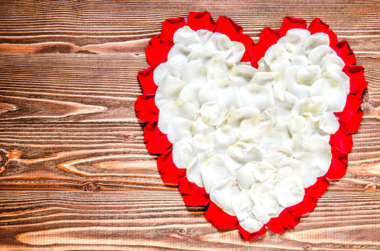 Heart of white and red rose petals on a wooden surface.
