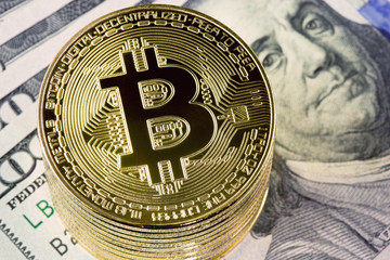 Metal bitcoin coins on one hundred dollar bills background.