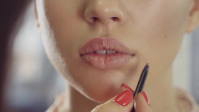 close shot on the face of a woman who is applied makeup on the lips, a lady make-up artist applies lipstick or eyeliner, hands have a manicure