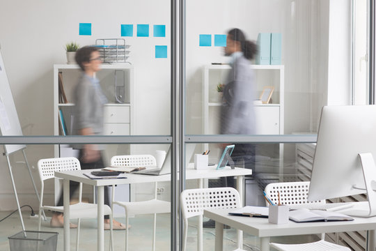Empty workplace of manager by transparent wall with moving office workers behind it