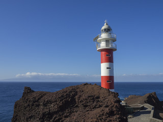 Fototapeta premium view on red white lighthouse on Punta de Teno cape on west Tenerife canary island with lava rock blue sea and clear summer sky