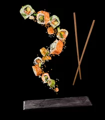 Fotobehang Flying pieces of sushi with wooden chopsticks and stone plate, isolated on black background. © Jag_cz