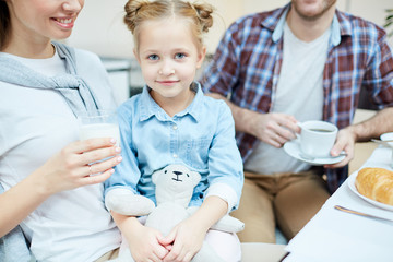 Obraz premium Adorable girl with teddie sitting on her mother knees with father near by