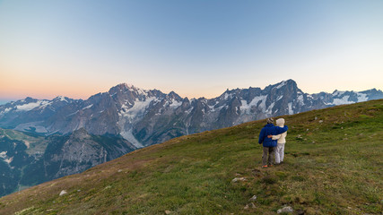 Fototapeta na wymiar Couple of people looking at the sunrise over Mont Blanc mountain peak (4810 m). Valle d'Aosta, italian summer adventures and travel destination on the Alps.