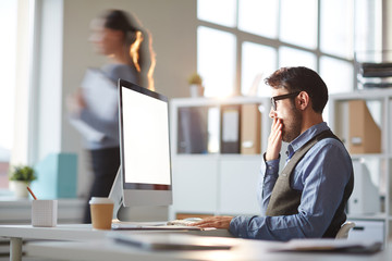 Businessman yawning by workplace while working in front of computer monitor