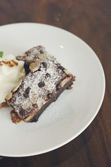 Rustic dessert background: brownies with almond, chocolate chip and whipped cream in white plate on dark wooden table. Text space