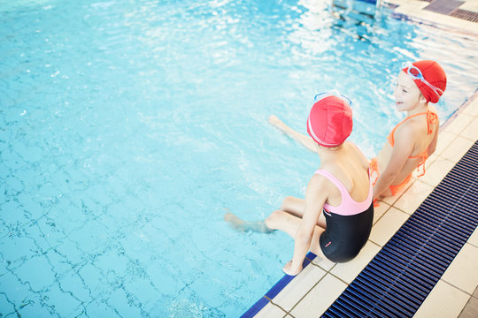 Happy and carefree schoolgirls spending leisure in swimming-pool and enjoying it