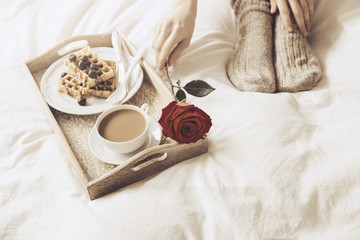 Woman taking rose from tray with breakfast