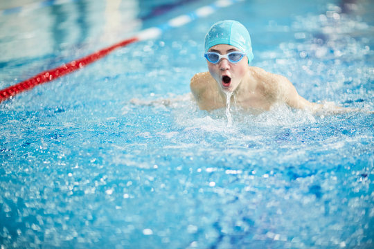 Skilled secondary schoolboy in swim-cap and goggles taking part in diving competition