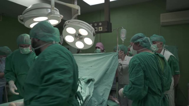 Teamwork of anesthetists, surgeons and medical workers performing surgical operation in operating room, patient lying on bed under anesthesia in sterile conditions, tracking, steady cam, interior 