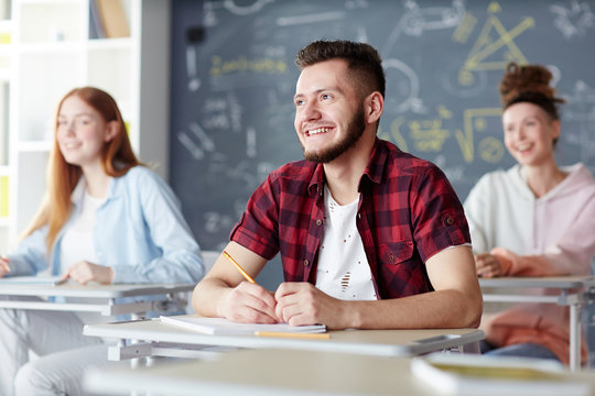 High-school learner looking at teacher with smile while listening to explanation at lesson