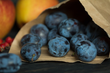 blue plums in a paper bag on a black wooden background