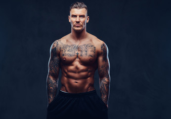 Fototapeta na wymiar A muscular tattooed man over dark background.