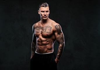 A muscular tattooed man on a dark background. - Powered by Adobe