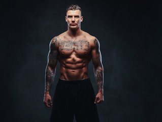 A muscular tattooed man on a dark background.