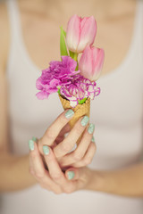 Obraz na płótnie Canvas woman hands holding spring flowers in an ice cream cone, sensual studio shot can be used as background