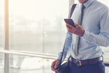 Portrait of a confident man. Entrepreneur working on phone while standing in modern office interior. Intelligent male lawyer holding phone. Businessman using cell phone in the airport terminal.