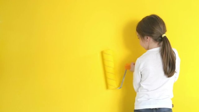 funny little girl gingerly paints the walls with a roller in the room