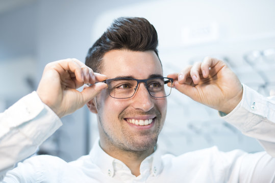 Man trying on glasses in optical store while smiling happy