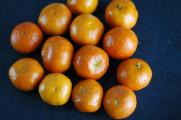 Unpeeled mandarins on a dark background with hard light.