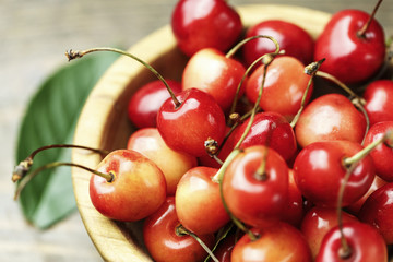 Ripe cherries with leaves on a wooden background, in a wooden plate, top view