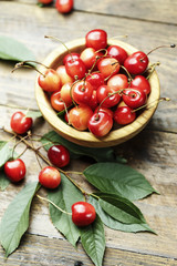 Ripe cherries with leaves on a wooden background, in a wooden plate, top view