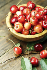 Ripe cherries with leaves on a wooden background, in a wooden plate, top view