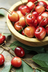 Ripe cherries with leaves on a wooden background, in a wooden plate, top view
