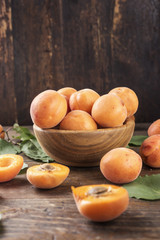 Fototapeta na wymiar ripe apricots with leaves in a wooden plate on a wooden background