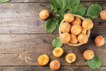 Naklejka na ściany i meble ripe apricots with leaves in a wooden plate on a wooden background