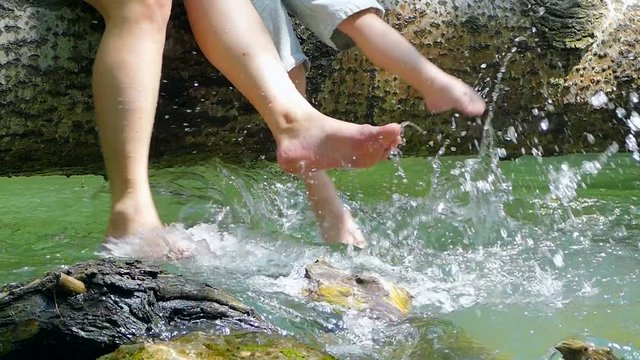 Several people play with their feet in the water on a fallen tree.