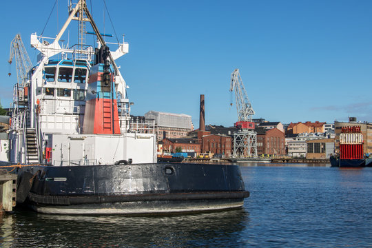 A motor boat anchoring in the harbor of Helsinki, on the background of a dock with cranes, Finland