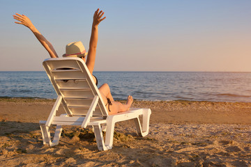 Relaxing at the beach in the evening, backside view. Rear view woman on chaise longue spreading hands wide.