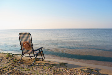 Sea landscape with deckchair and sun hat. Transparent sea water.