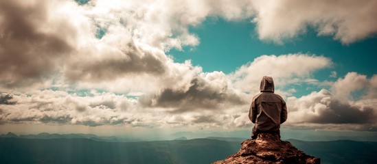 Lonely man sitting on top of mountain cloudy sky - Powered by Adobe