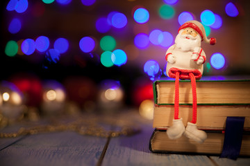 Toy Santa Klaus with a gift sits on the books on the background bokeh